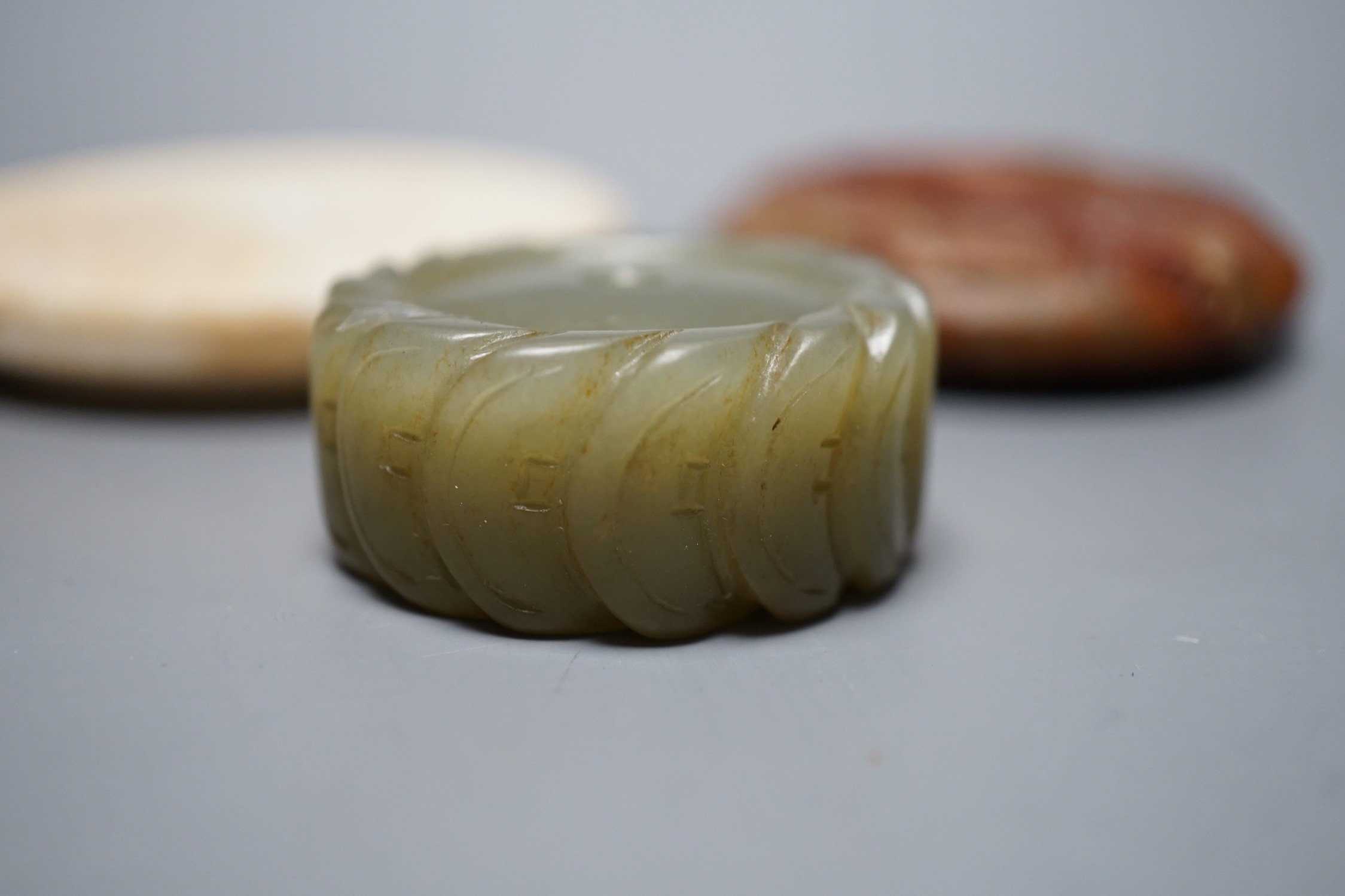 A Chinese green jade 'cash' pendant, a russet jade bi-disc and a burnt jade circular plaque